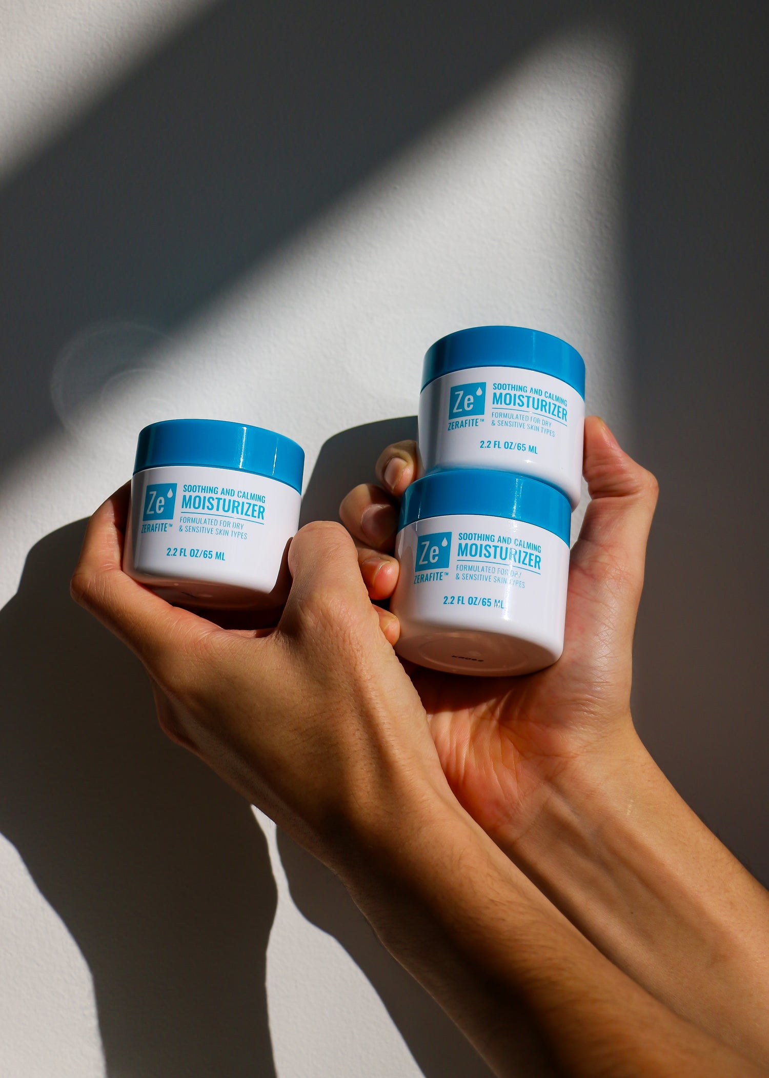 Two hands holding jars of Zerafite Soothing and Calming moisturizer against a neutral background