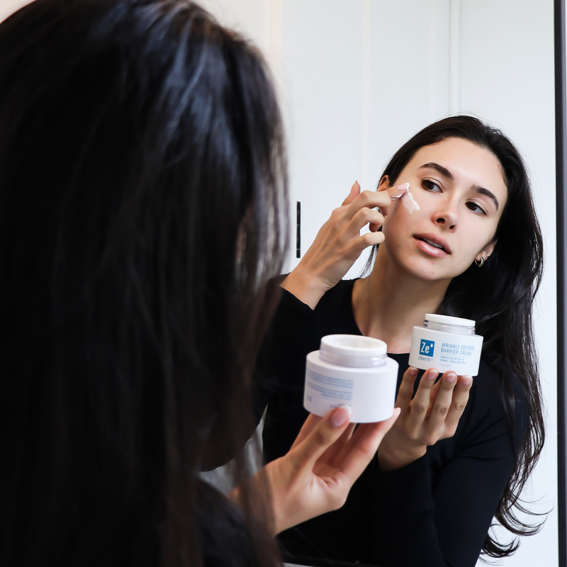 Woman applying cream to her face in front of a mirror