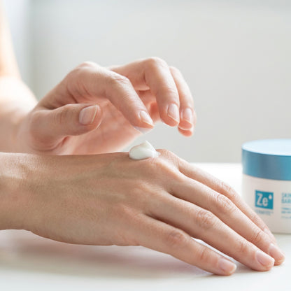 Two hands smoothing Zerafite Skin Brightening Barrier Cream into the back of one hand, the jar alongside.