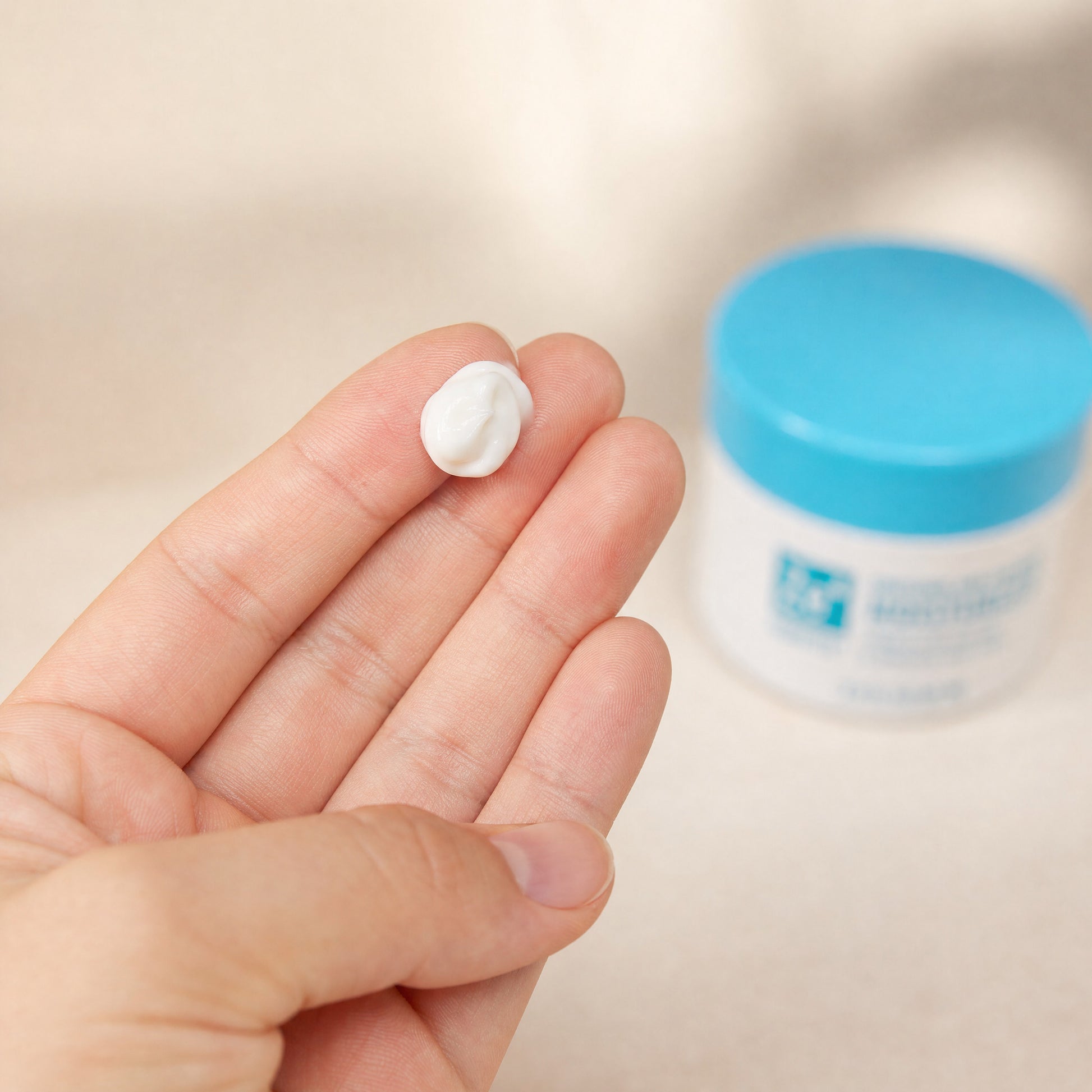 A fingertip holding a small dollop of Zerafite Soothing and Calming Moisturizer, the jar behind.